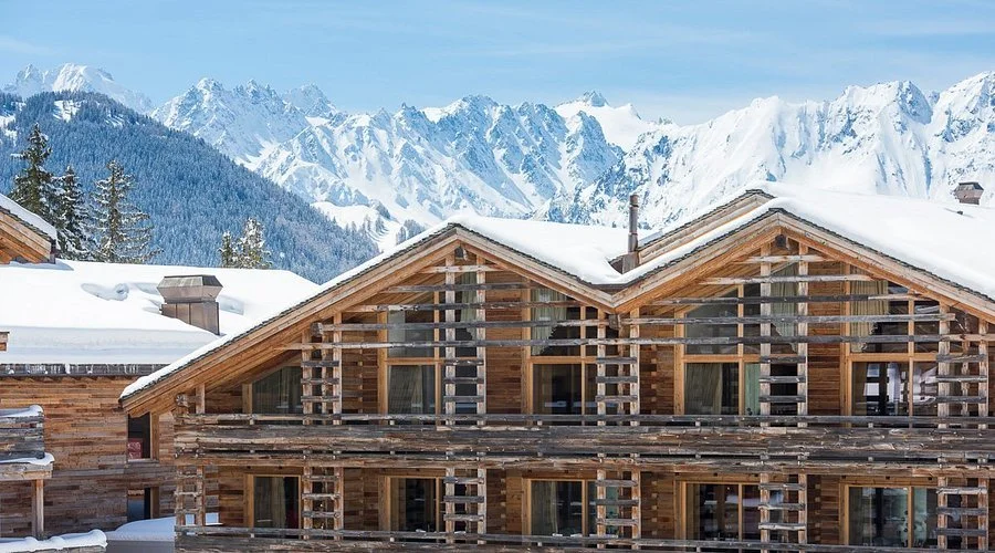 Façade extérieure du luxueux hôtel W Verbier dans le Valais suisse. Le design moderne en bois s’intègre au paysage enneigé, avec des montagnes alpines imposantes en arrière-plan, idéal pour un séminaire Aylo Montagne.
