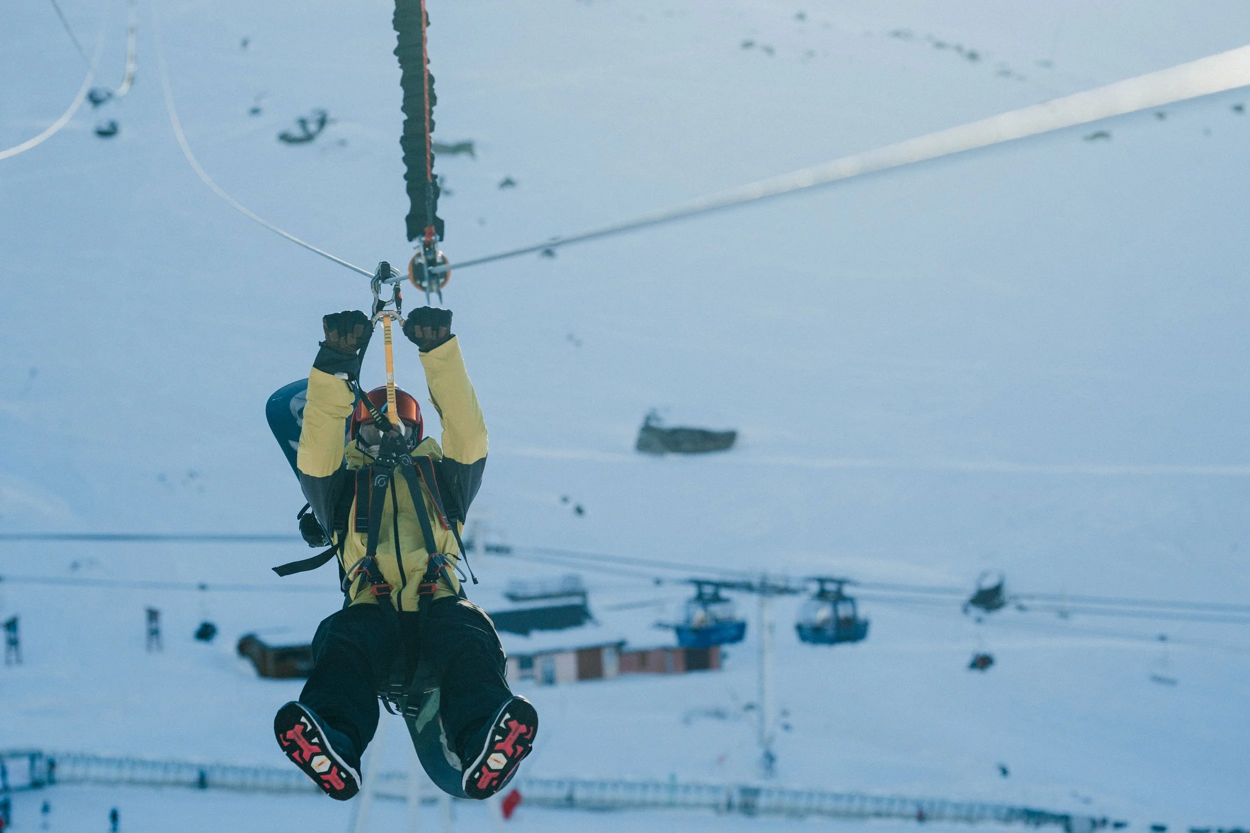 Une personne en tenue de ski dévalant une pente enneigée en utilisant un équipement de ski de randonnée ou de ski alpin, avec des bâtiments en arrière-plan et une ambiance hivernale.