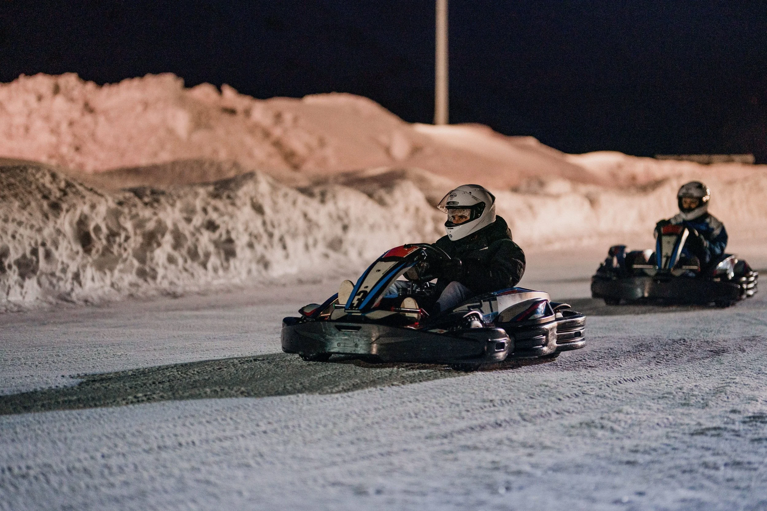 Deux personnes conduisant des kartings sur une piste enneigée la nuit.