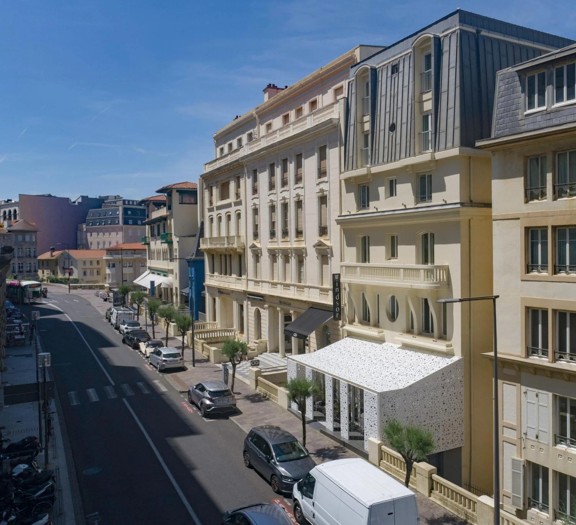 Façade de l’Hôtel Windsor Biarritz, un bâtiment classique dans le centre-ville. Un toit blanc moderne à l’entrée crée un contraste architectural unique dans la rue.