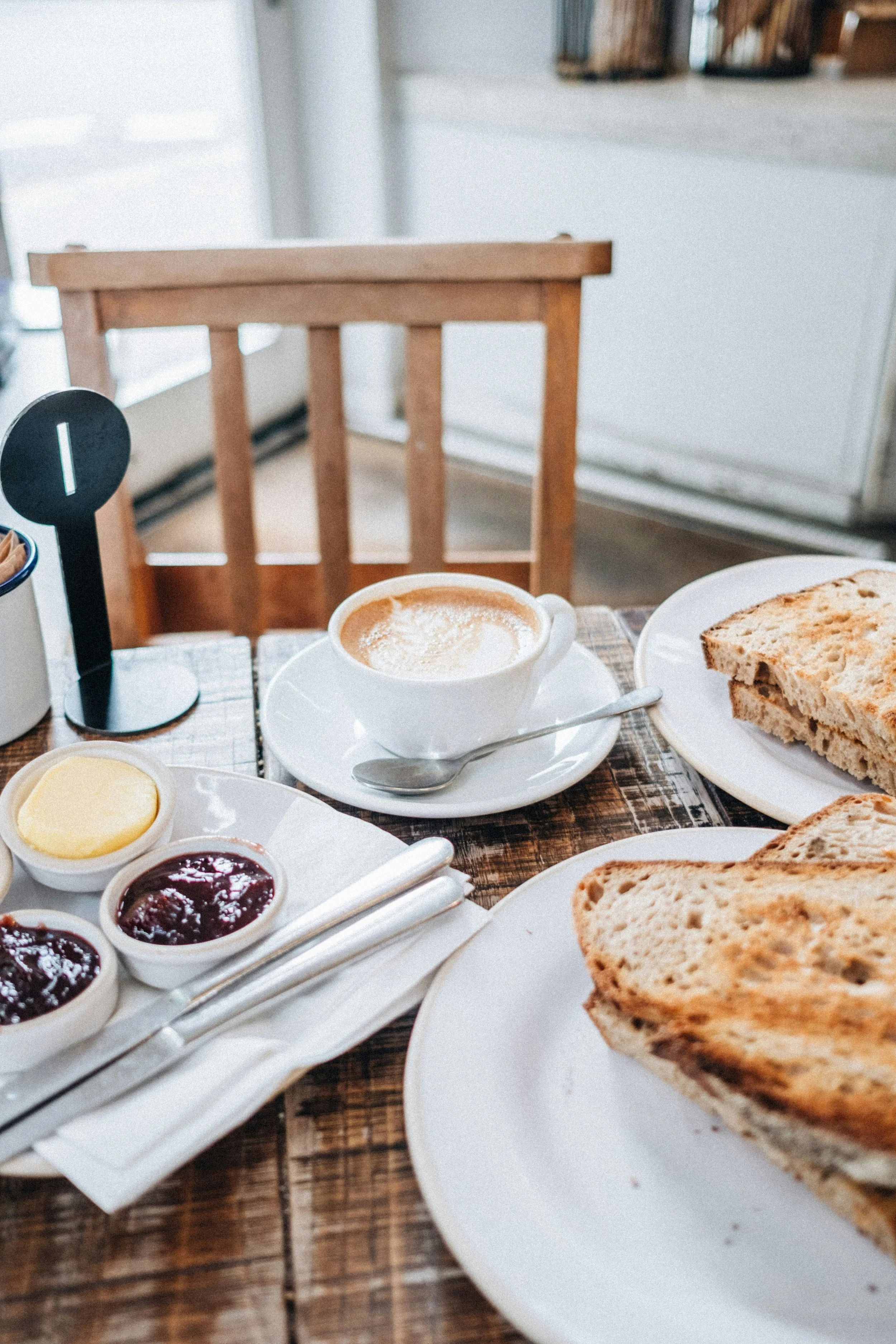 Mise en place pour le petit-déjeuner : café, tartines grillées et confitures sur une table en bois, représentant un moment convivial et la qualité du service hôtelier.