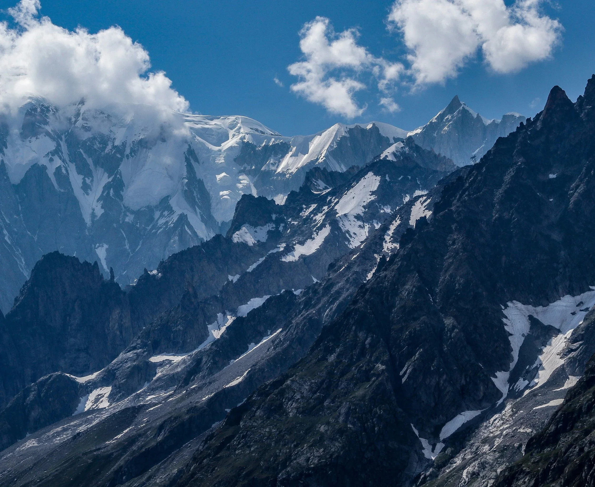 Montagnes enneigées avec des sommets pointus, ciel bleu avec quelques nuages.