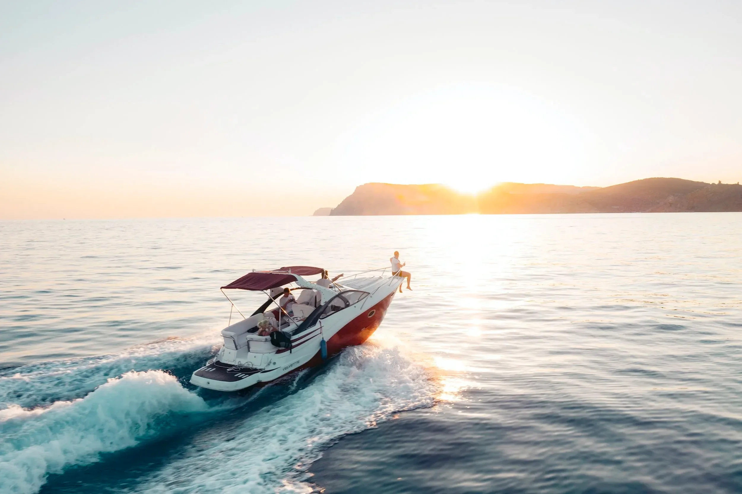 Un bateau à moteur naviguant sur la mer au coucher du soleil avec des collines en arrière-plan.