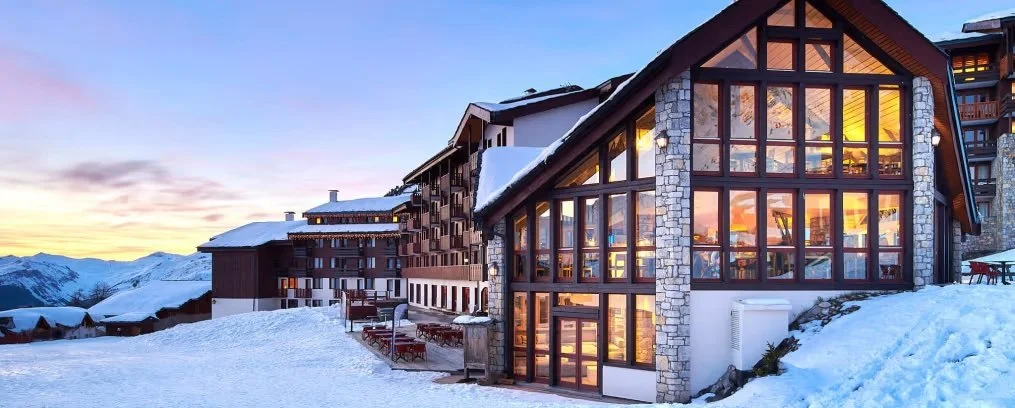 Façade nocturne de l’hôtel L’Eden des Cimes à La Plagne, un grand chalet au design moderne en pierre et aux grandes baies vitrées, créant une ambiance chaleureuse dans la neige.