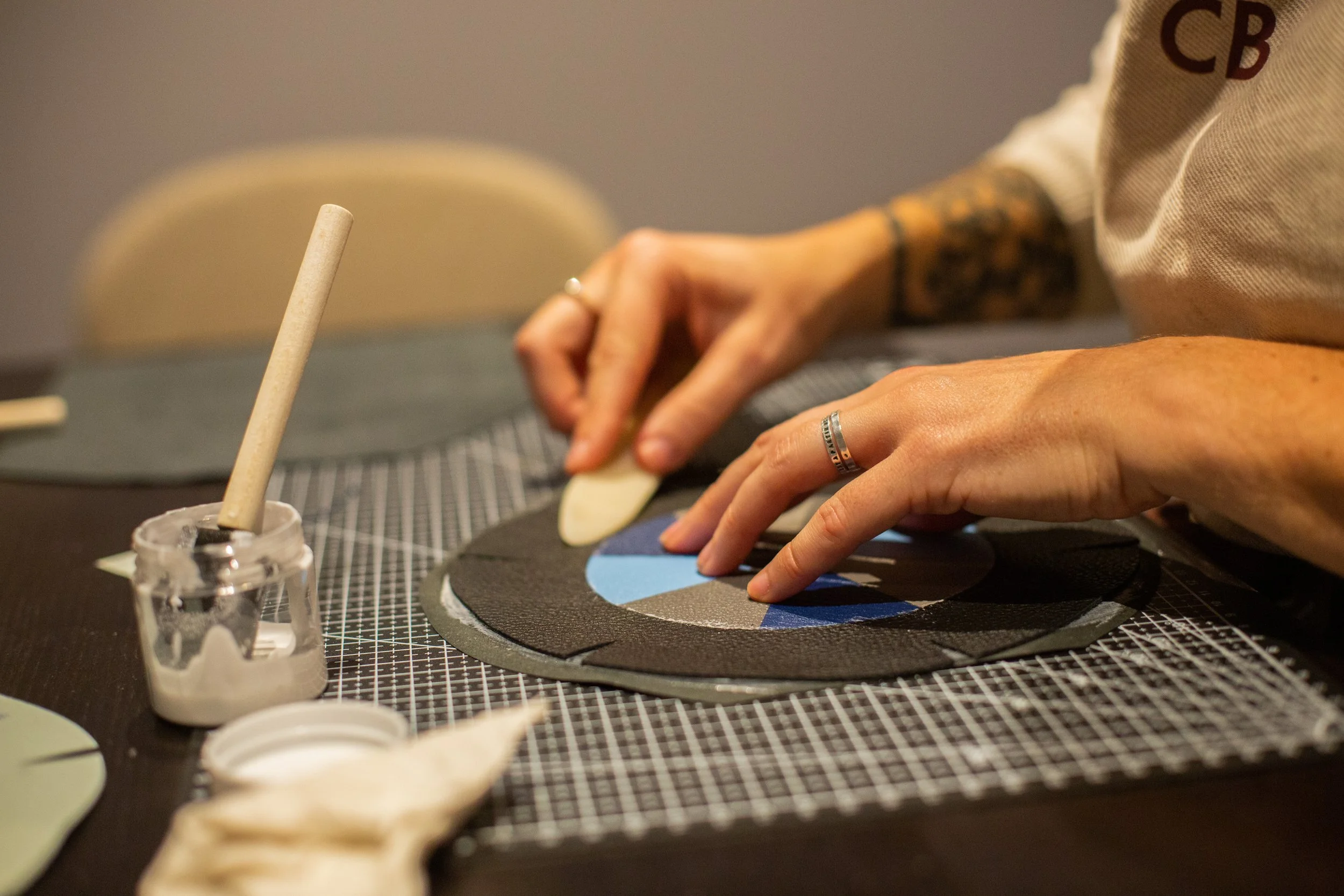 Une personne crée une pièce en céramique ou en cuir, utilisant des outils et des matériaux de travail artistiques, avec un focus sur ses mains et une surface de travail.