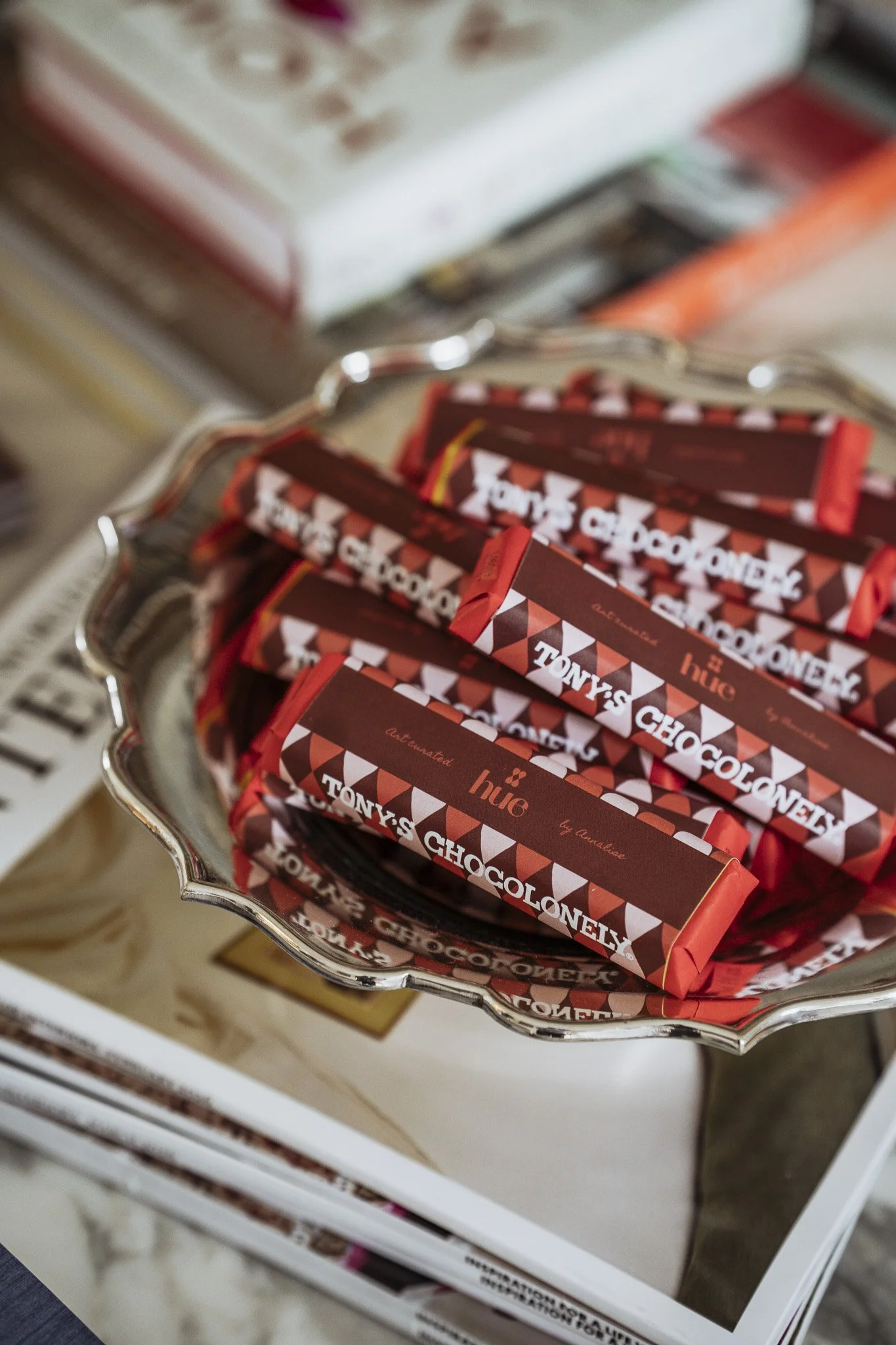 A close-up view of a silver tray filled with Tony's Chocolonely chocolate bars in red packaging with white and black text, placed on a display shelf in a store.