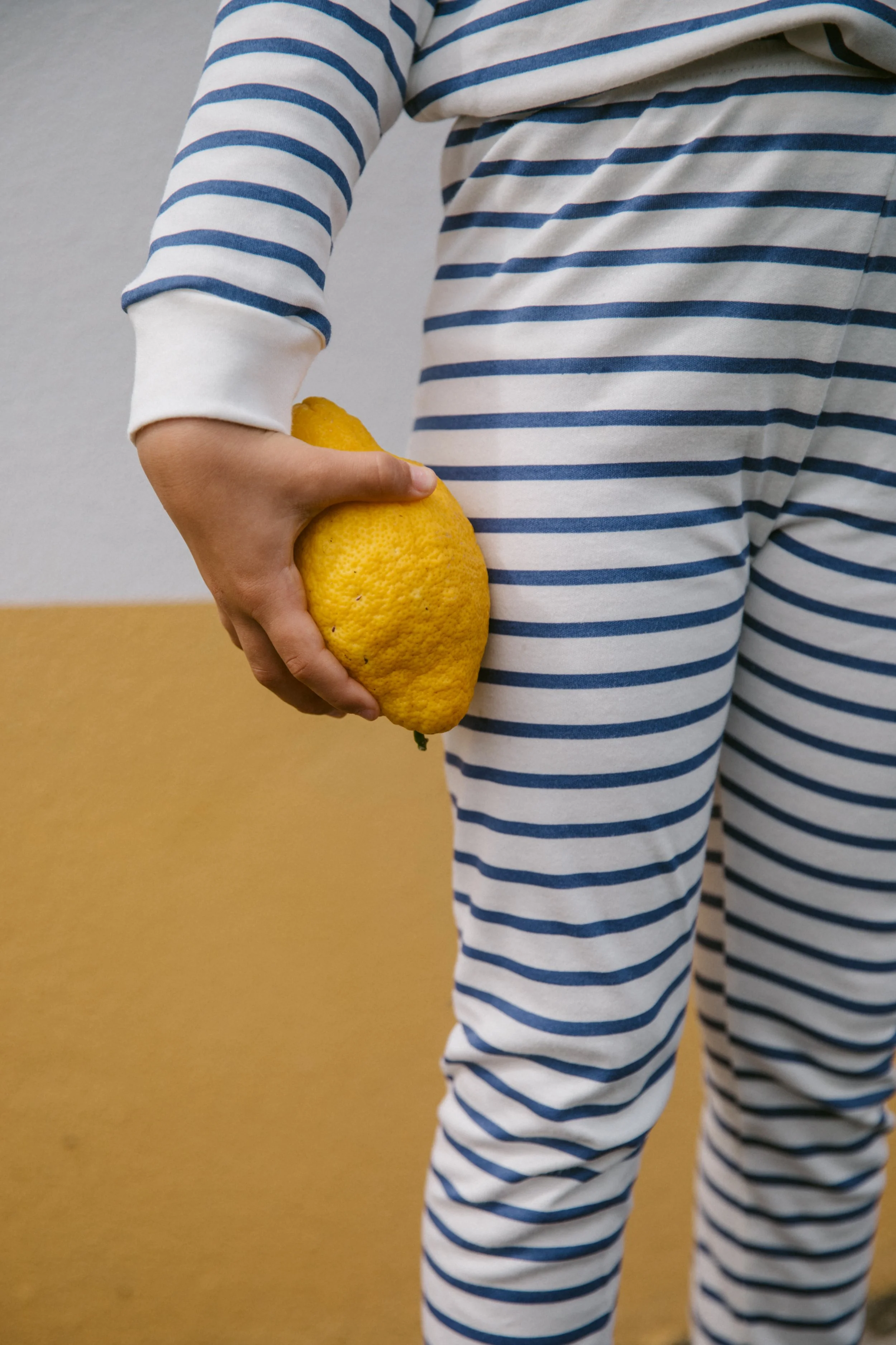 Person wearing a striped pajama set holding a yellow lemon behind their back.