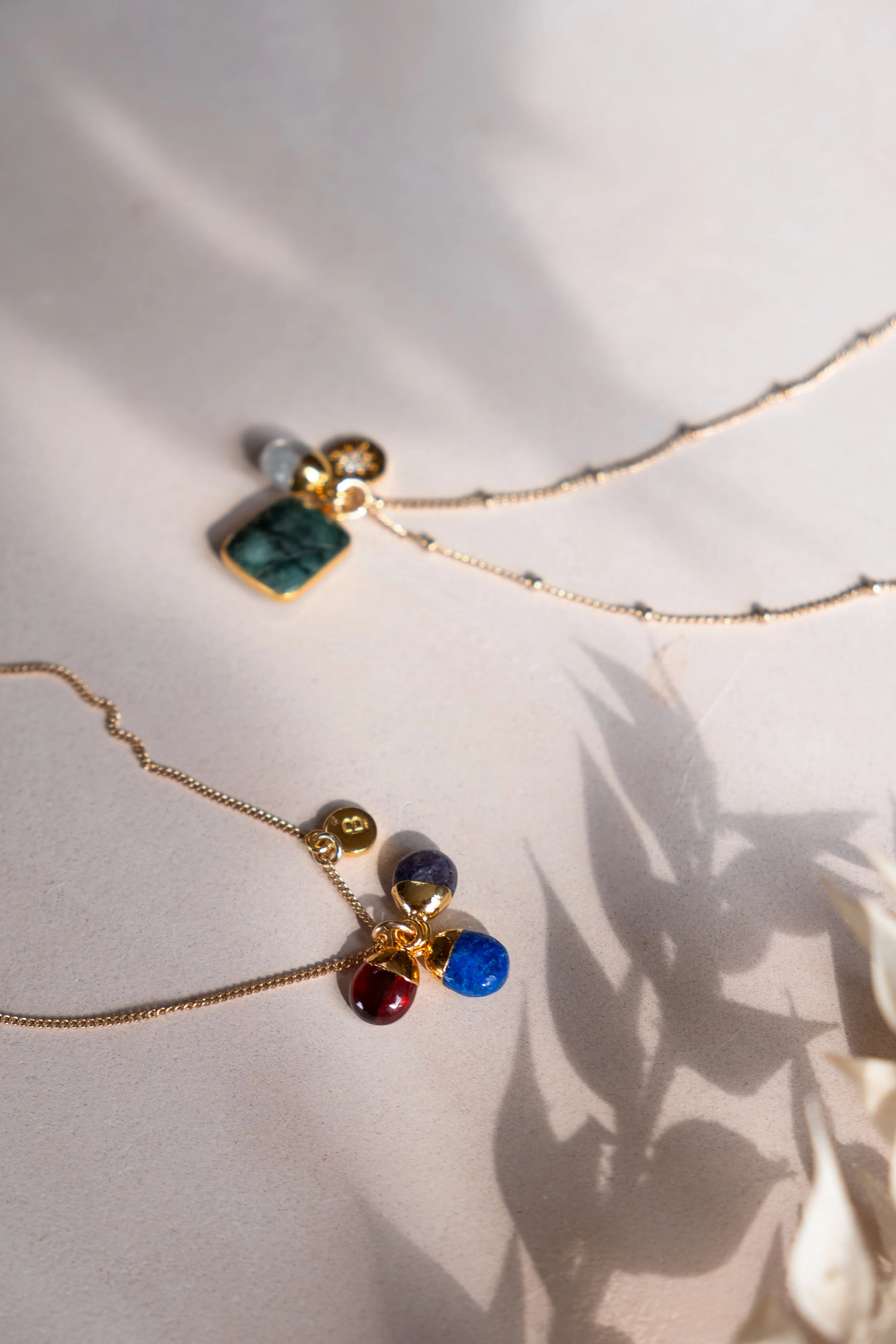 Close-up of colorful gemstone necklaces with gold chains lying on a white surface, casting shadows.