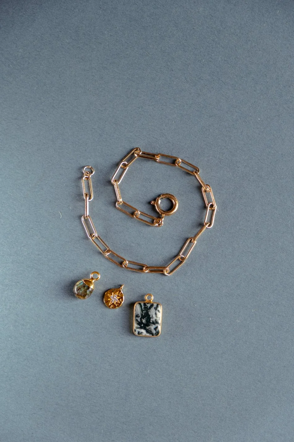 Gold chain necklace, silver chain bracelet, and three pendants with stones on a gray background.
