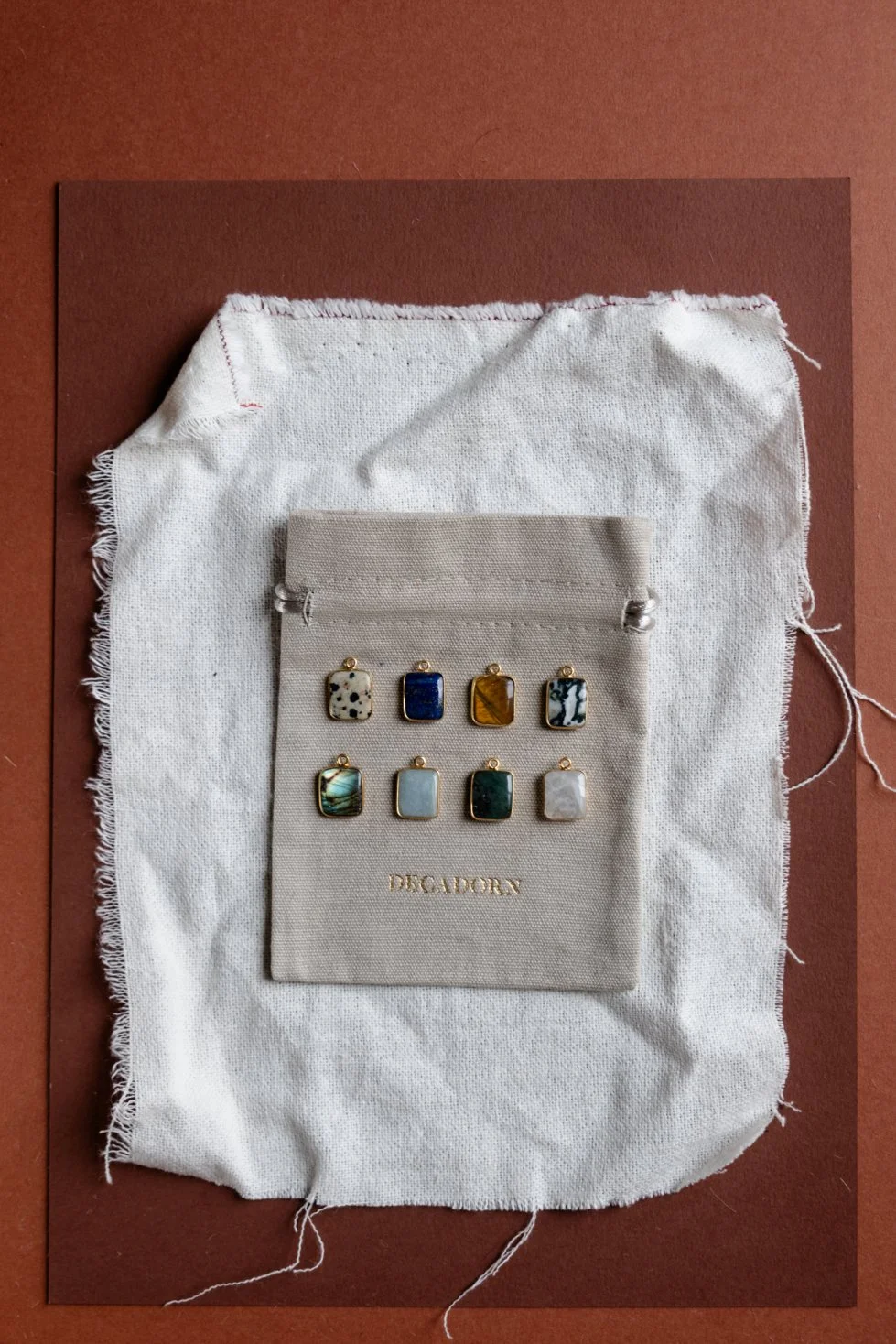 Set of eight jewellery pendants with various stone designs on a jewelry card, displayed on a fabric pouch on a brown background.