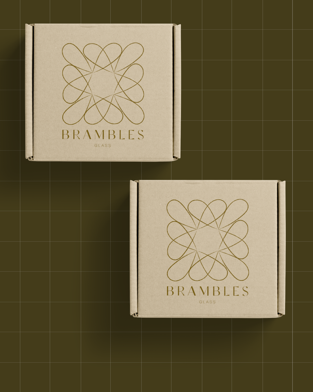 Two beige boxes with gold geometric design and the text 'BRAMBLES GLASS' on the top surface, placed on a dark green grid background.