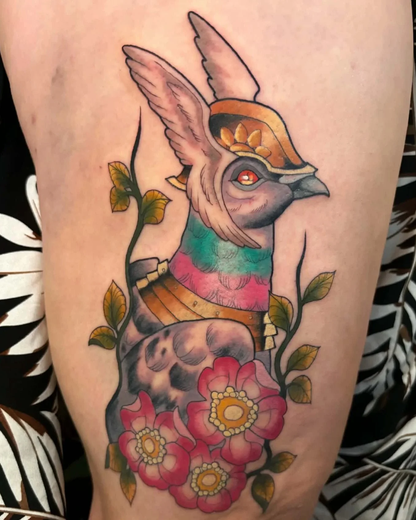 Colorful tattoo of a mythical bird with floral and foliage elements on skin.
