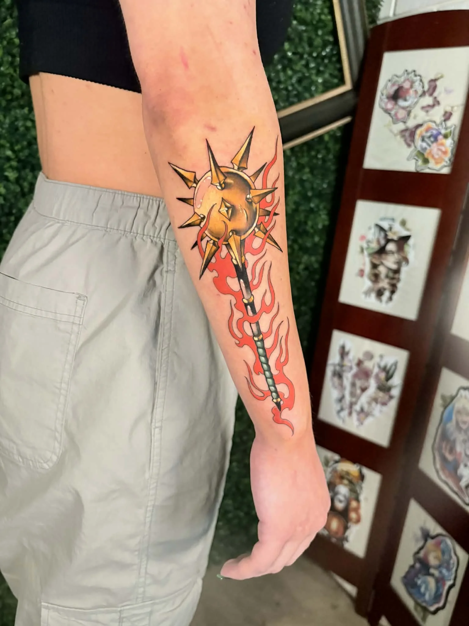 Colorful tattoo of a flaming, spiked mace on a person's forearm.
