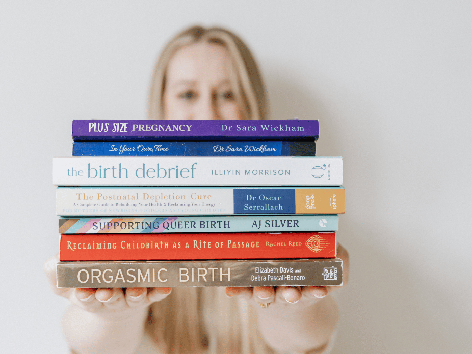 Person holding a stack of seven books about pregnancy and childbirth.