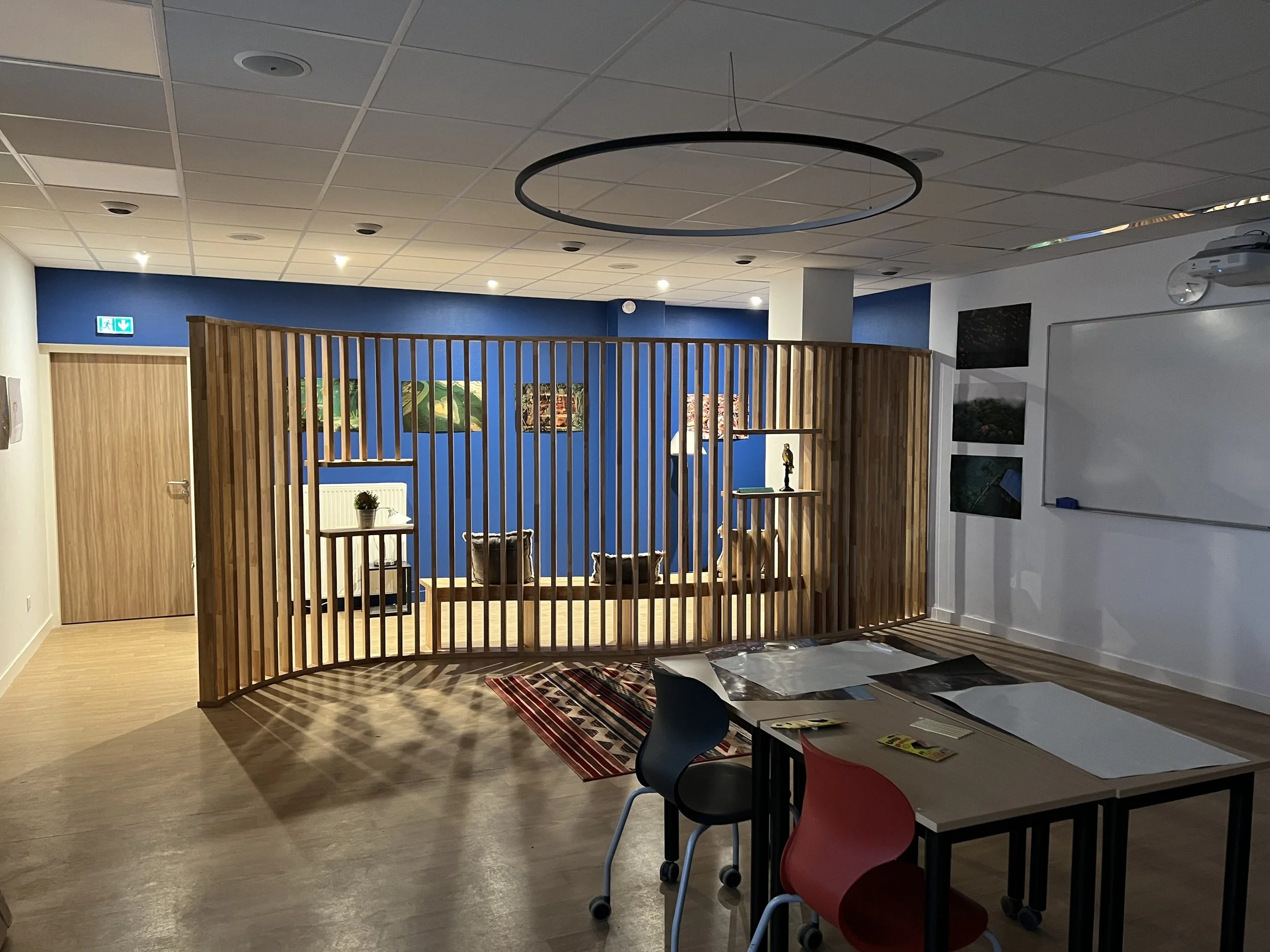 Salle de réunion ou espace d'accueil avec un mur bleu, des fauteuils, une cloison en bois et des peintures murales.