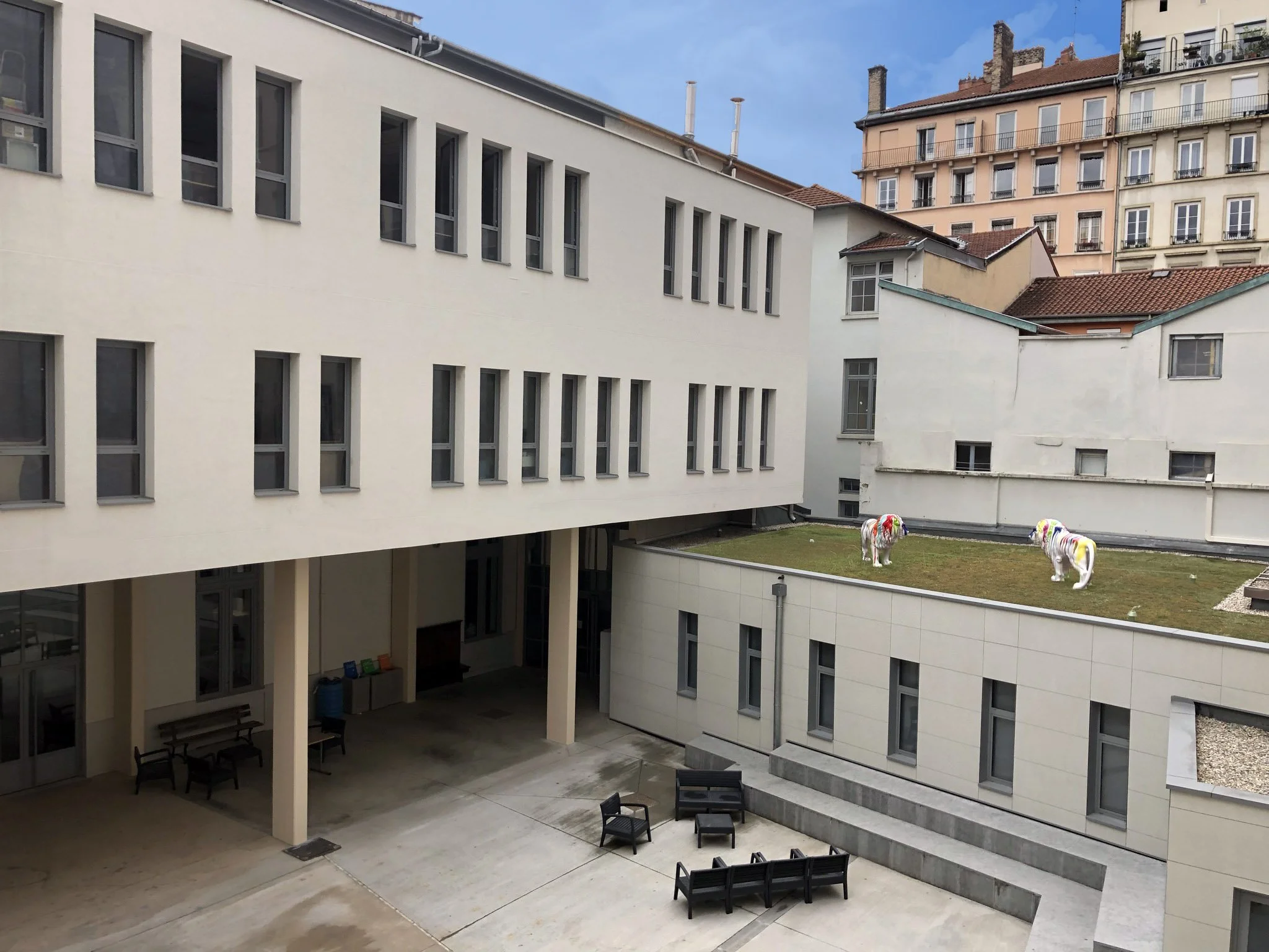 Vue d'un couloir intérieur d'un bâtiment moderne avec des fenêtres, une zone de repos avec des bancs et deux sculptures de chevaux en arrière-plan sur un toit vert.