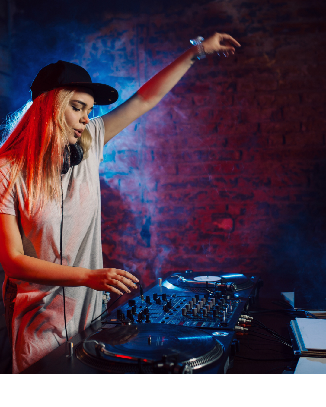 Une DJ femme avec des cheveux blonds et une casquette noire, jouant avec un équipement de DJ dans un club avec un éclairage coloré.