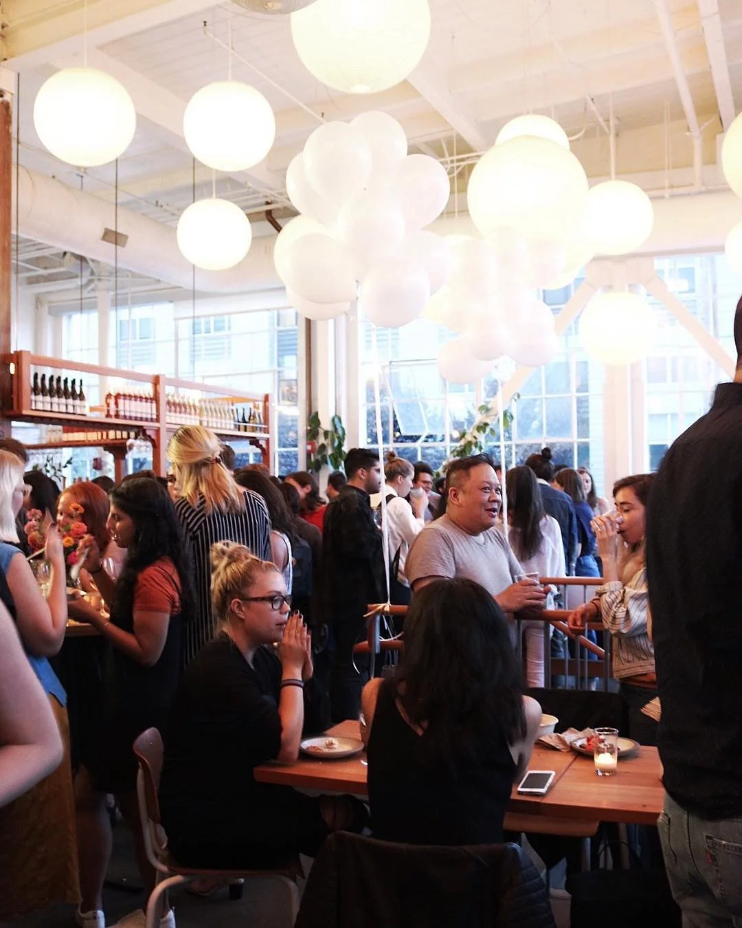Une foule de personnes présente pour une inauguration dans un restaurant ou un café, avec des décorations lumineuses suspendues au plafond, et un mobilier en bois.