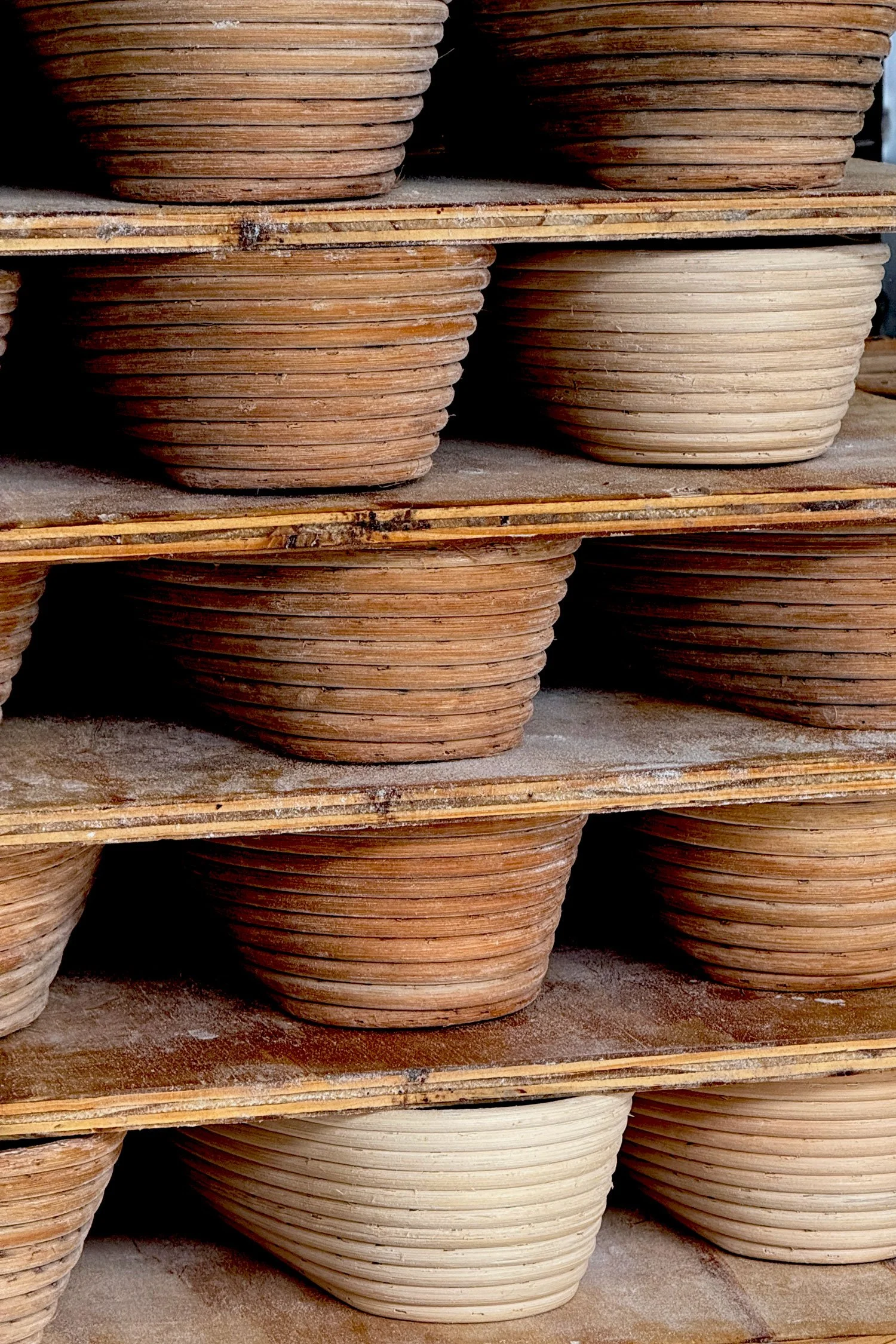 Estantes llenas de cestas apiladas, cestas para que repose la masa madre, algunas son de color marrón y otras beige.