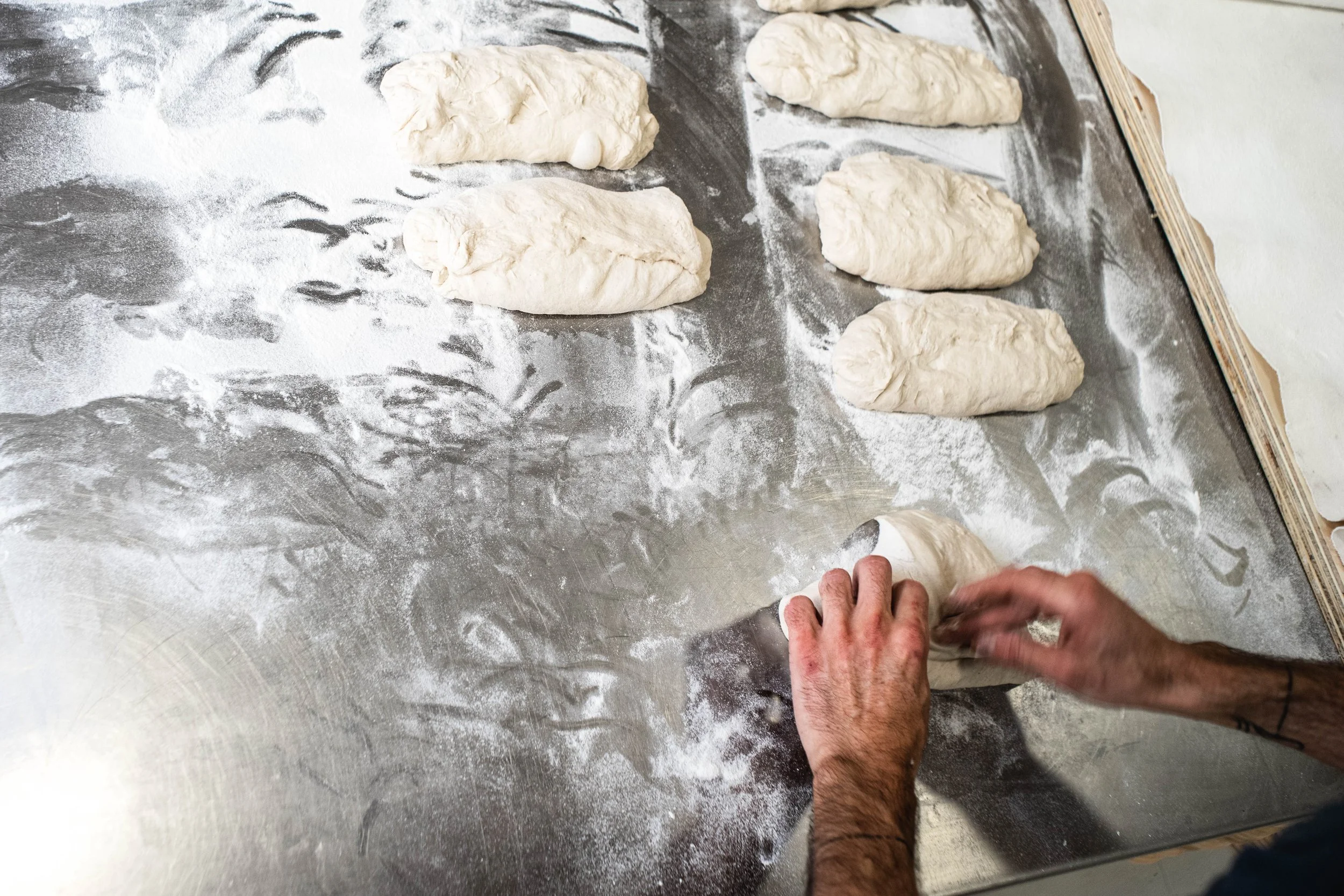 Persona formando bollos de masa sobre mesa en proceso de panadería.