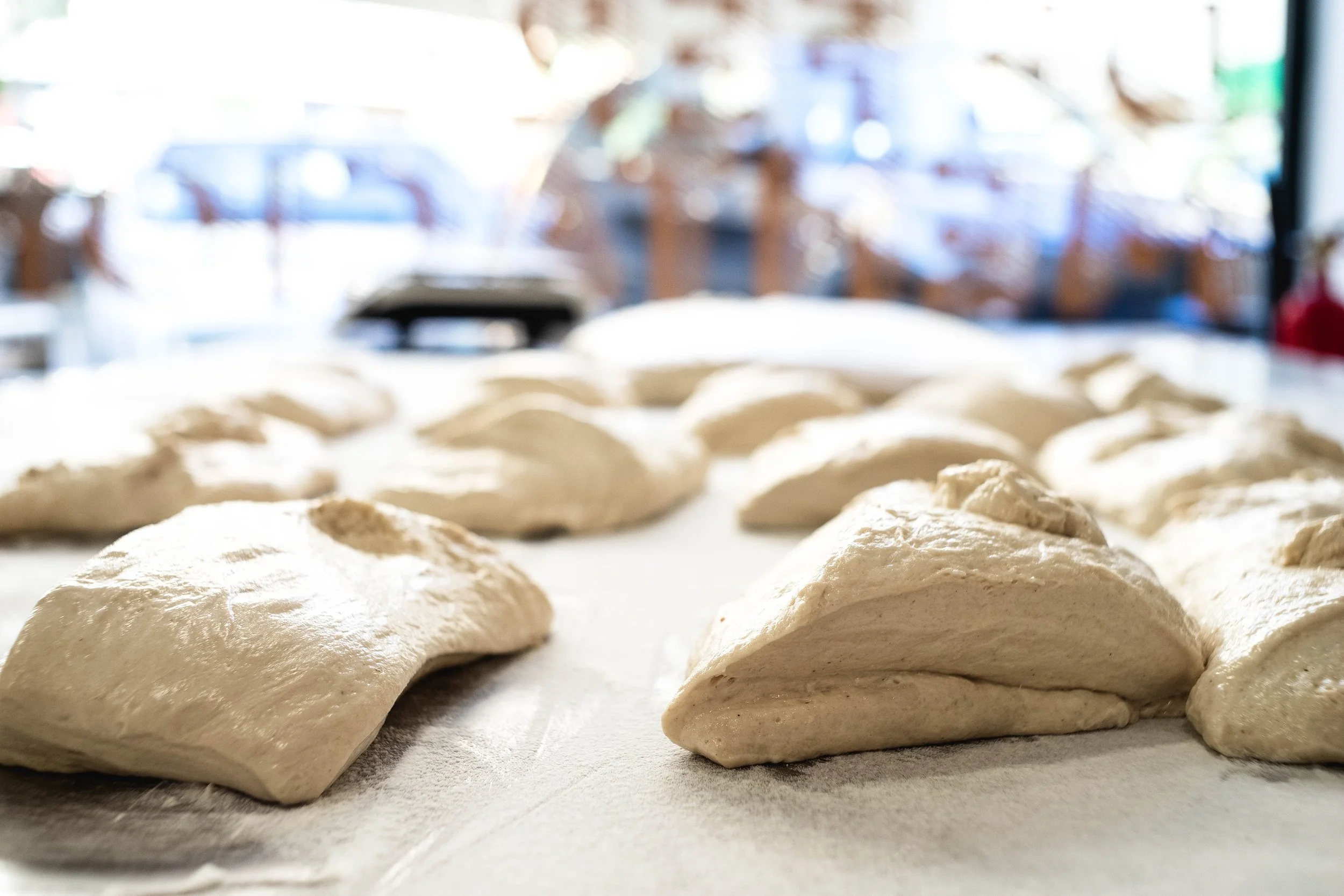 Masa de masa de pan en proceso de fermentación, en una mesa, con fondo difuminado de una panadería.