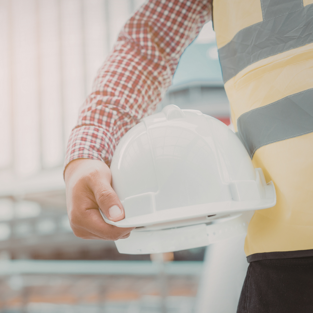 Person holding a white safety helmet, dressed in a yellow safety vest and red checkered shirt, at a construction site. Having a meeting with an Advisor