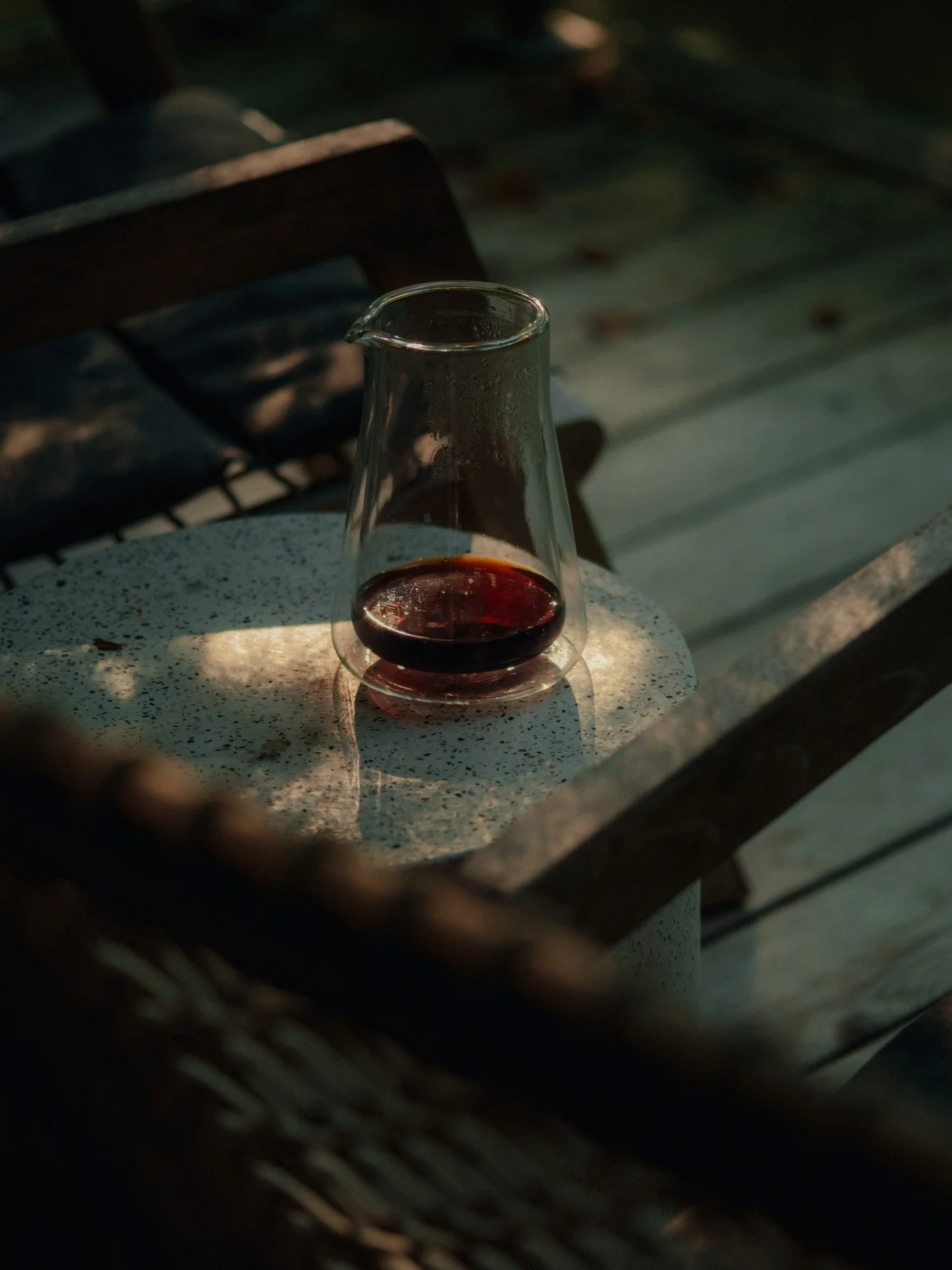 A glass of red wine on a speckled white table, with a shadow cast across it, outside on a deck or patio.