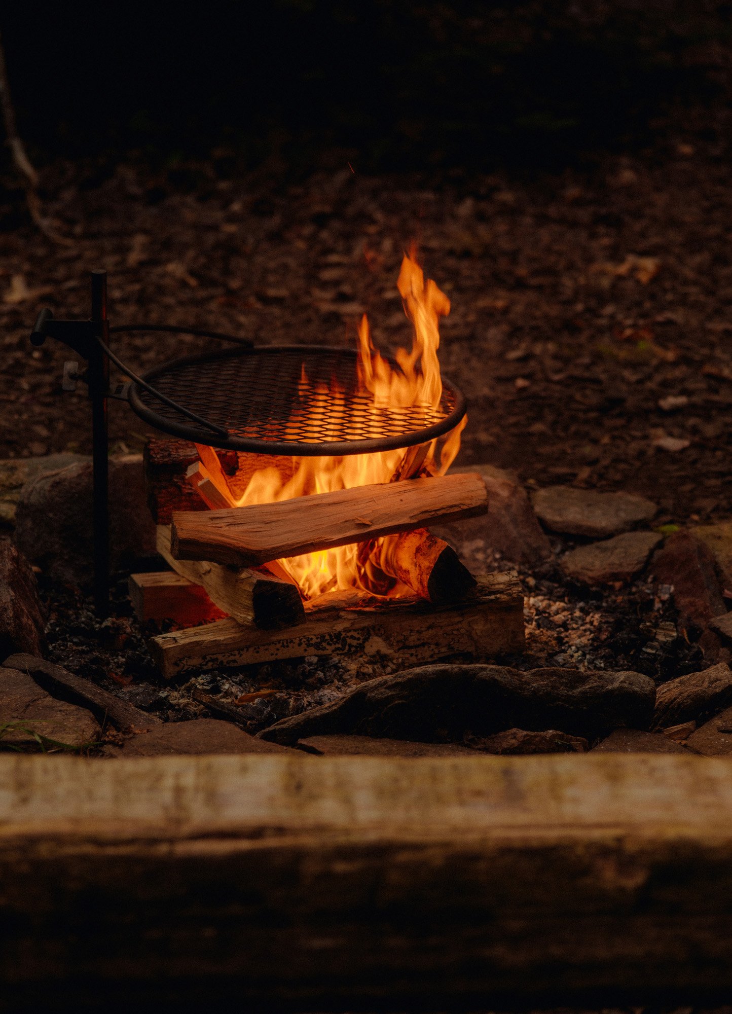 Campfire with split logs and a grilling grate, set outdoors at night.