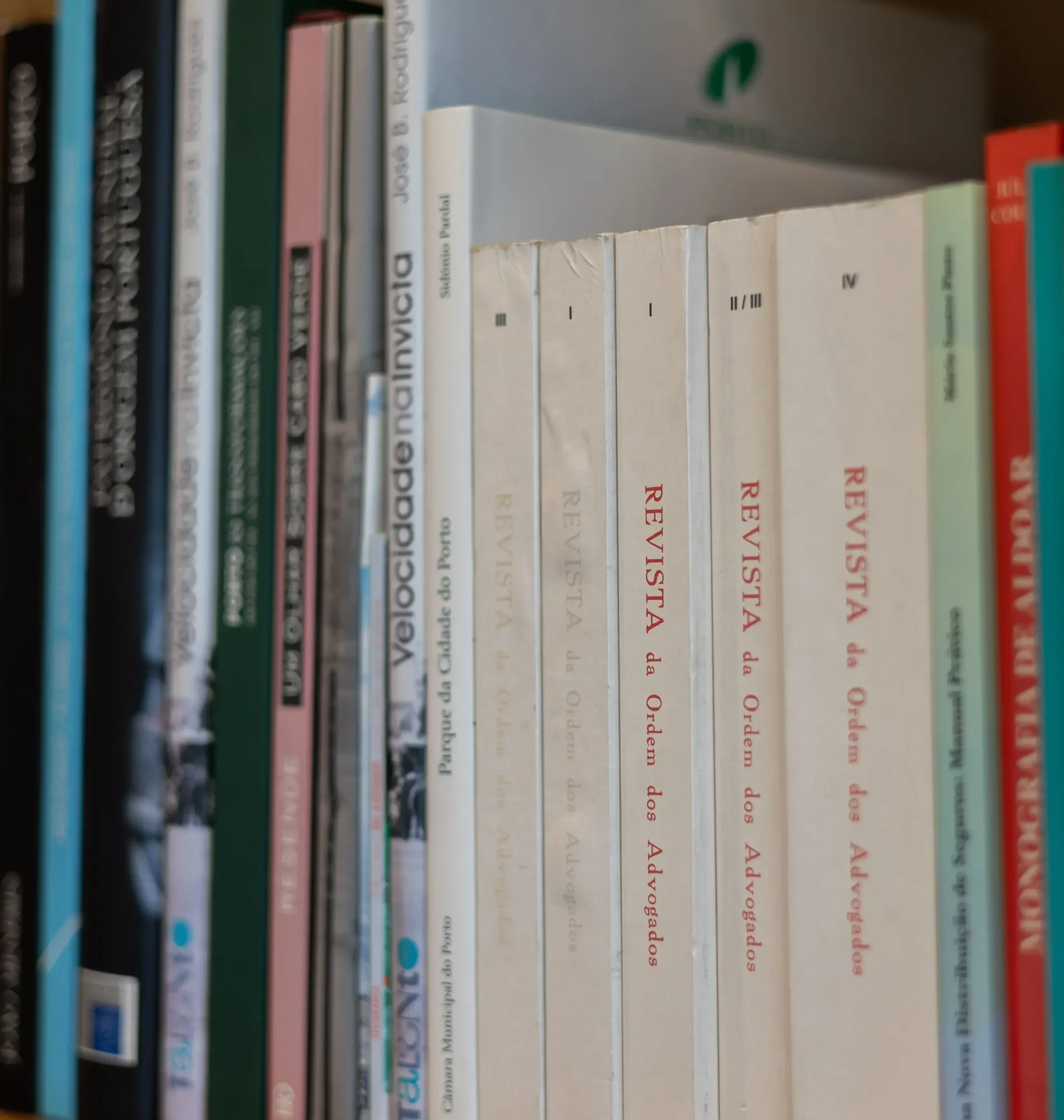A bookshelf with books, including titles in Portuguese and English, some titles visible are 'Velocidade na Inveja,' 'Revisita da Ordem dos Advogados,' and 'Respostas.'