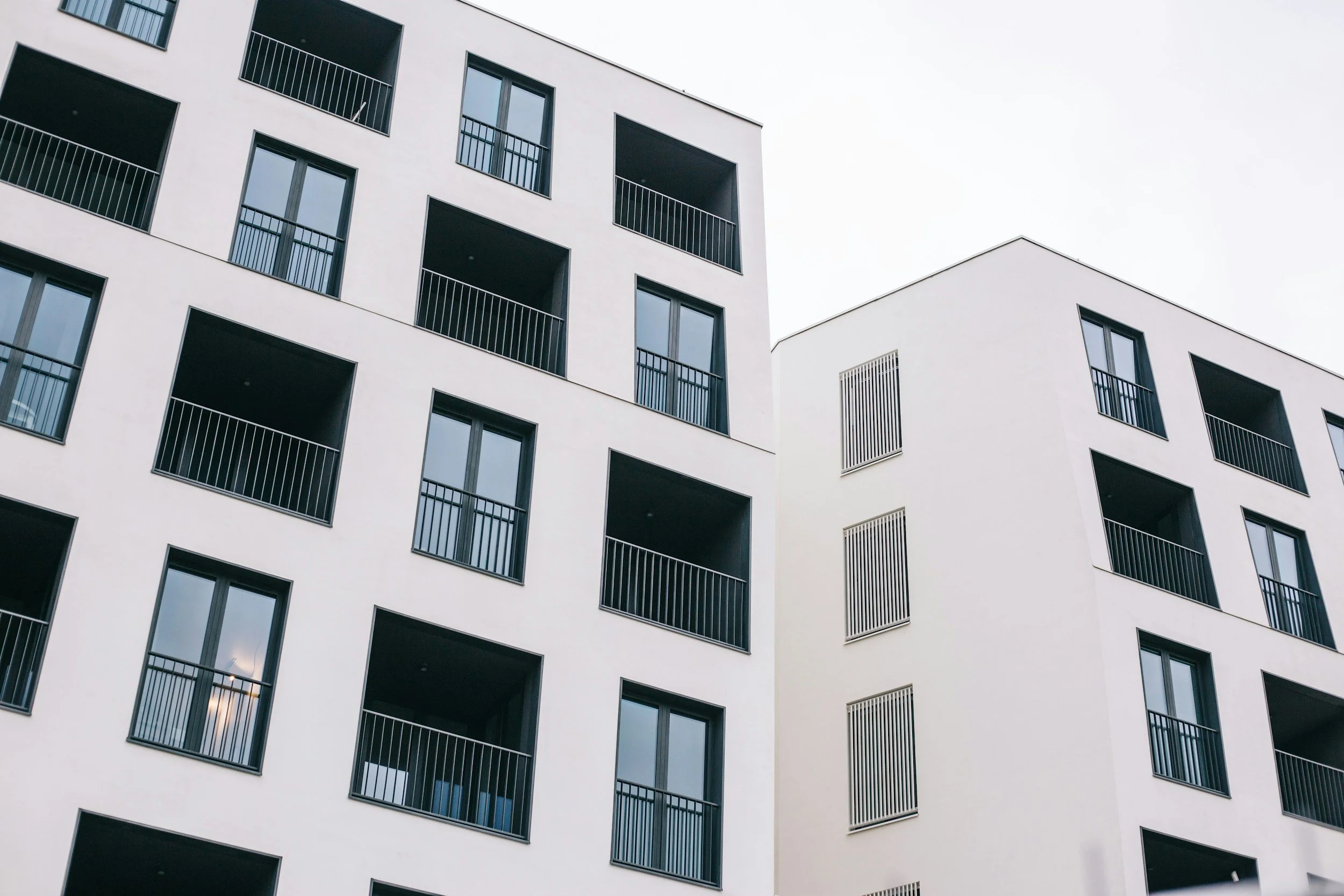 View of modern white apartment buildings with black-framed windows and balconies, feature simplistic design, on an overcast day.