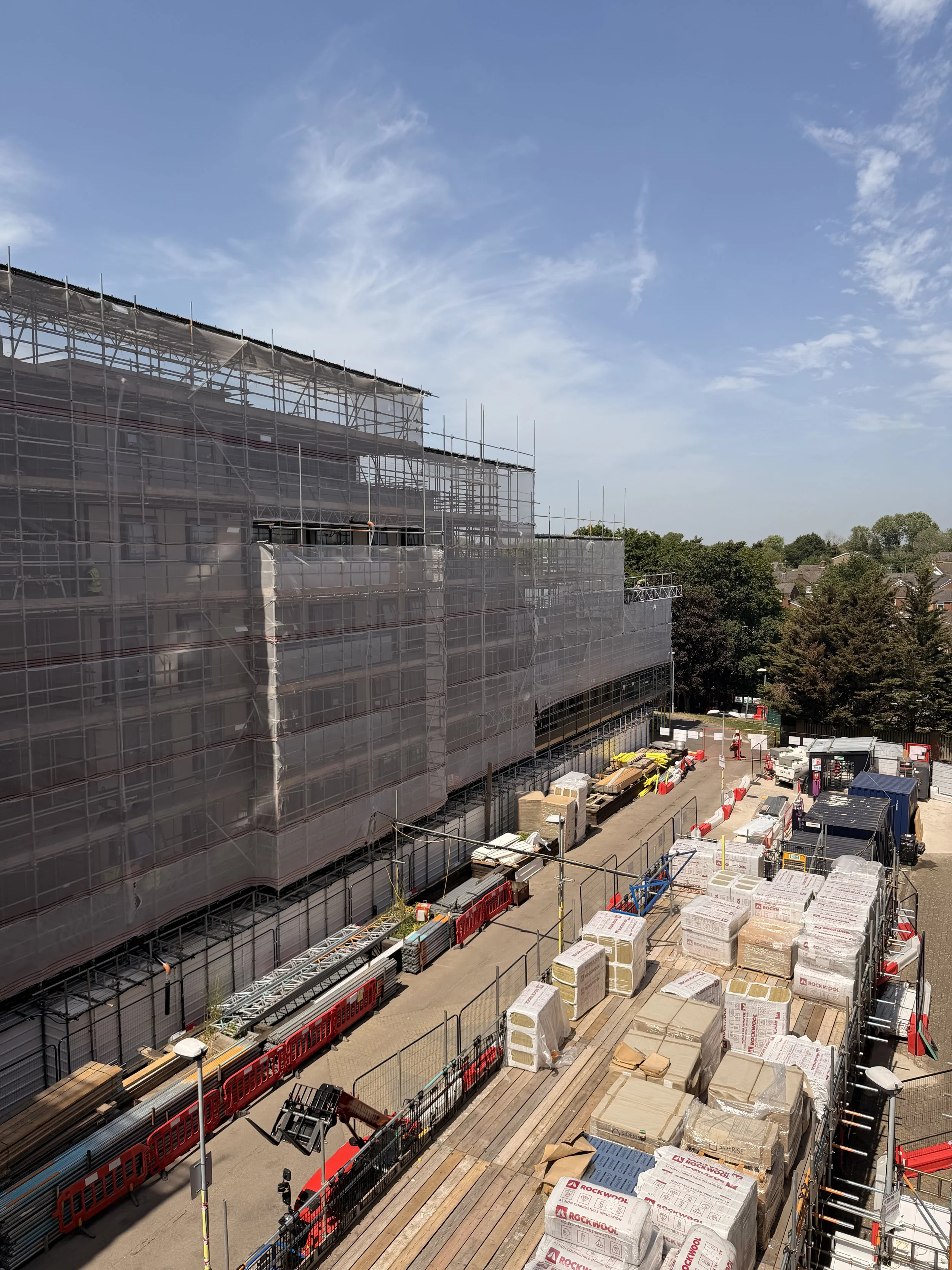 Construction site with scaffolding on a building, construction materials and supplies on the ground, and a clear blue sky.