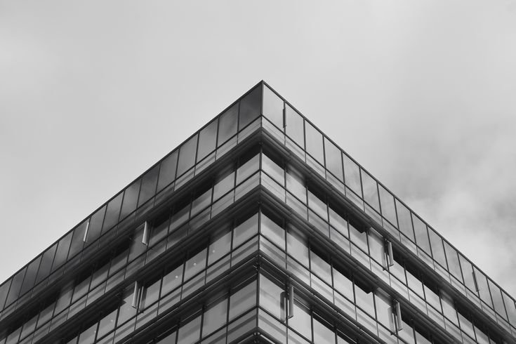 Black and white photo of the corner of a modern glass building with overcast sky in the background.