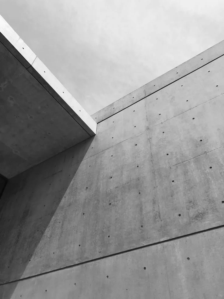 Black and white photograph of modern concrete building walls and ceiling seen from below, with architectural angles and lines.