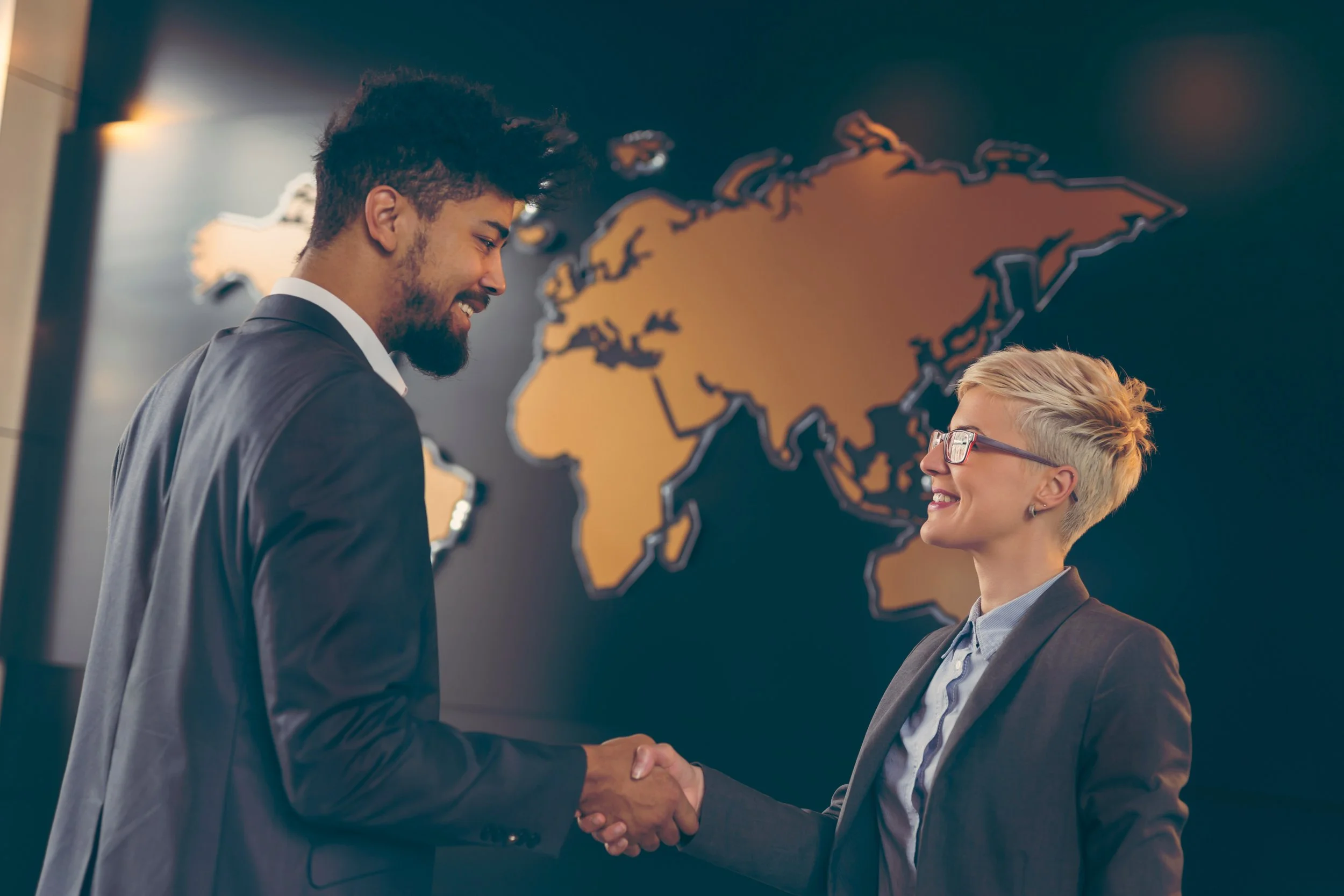 Business partners shaking hands in front of a world map, representing an international business partnership.