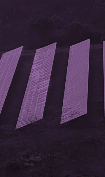 Several vertical pieces of paper or fabric hung on a line outdoors at night, illuminated with purple light.