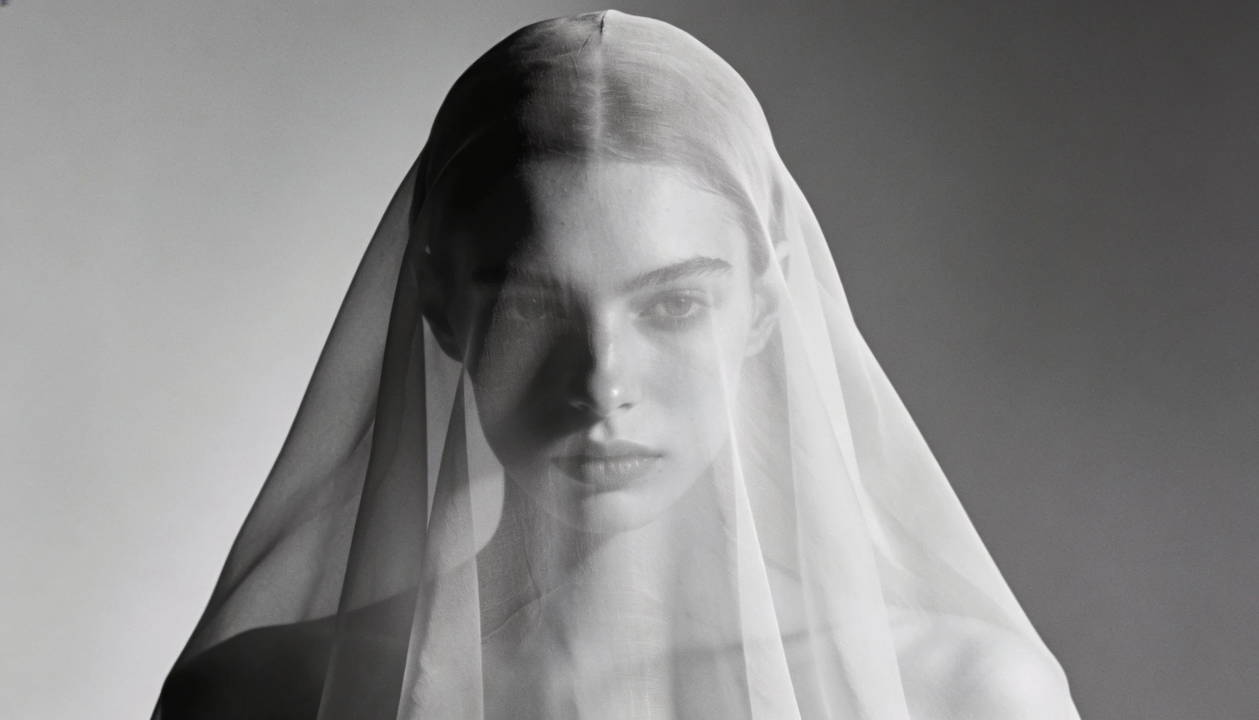 Schwarz-weiße Fotografie eines jungen Frauengesichts mit einem halbtransparenten Schleier, der das Gesicht teilweise verdeckt.