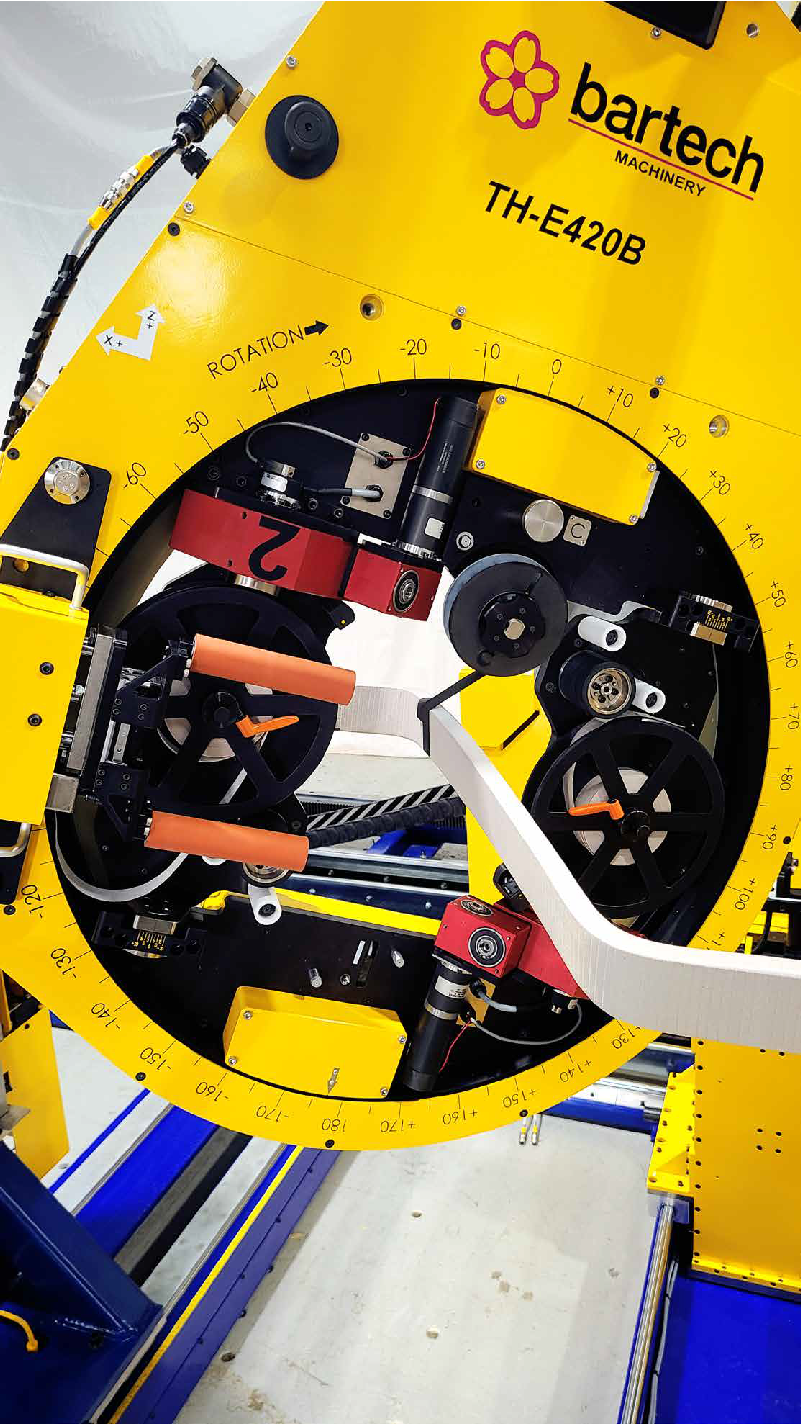 Close-up of a yellow bartech machinery with various gears, wheels, and measurement markings, featuring a decorative flower logo and the model number TH-E420B.