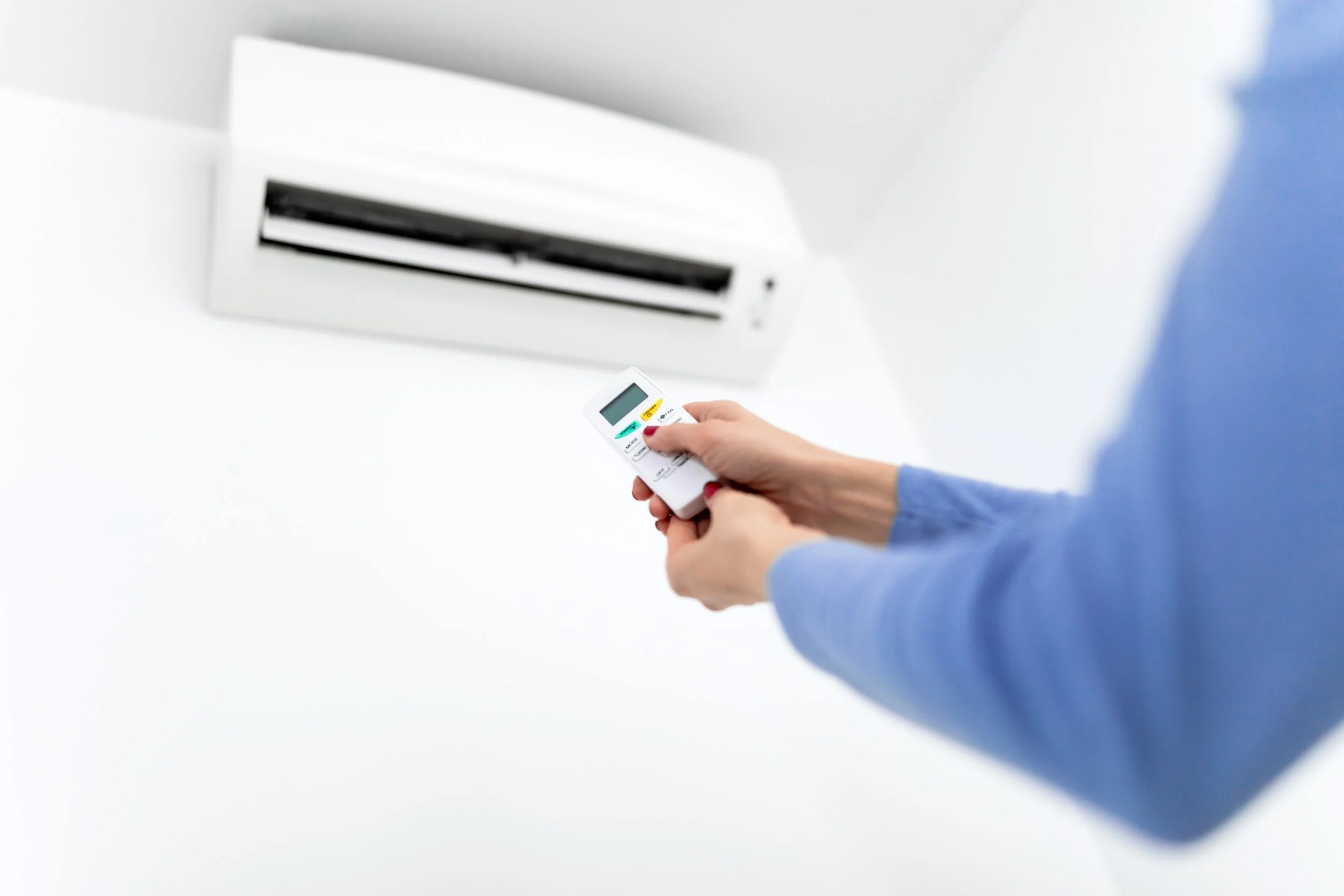 Person adjusting or turning on an air conditioning unit with a remote control.