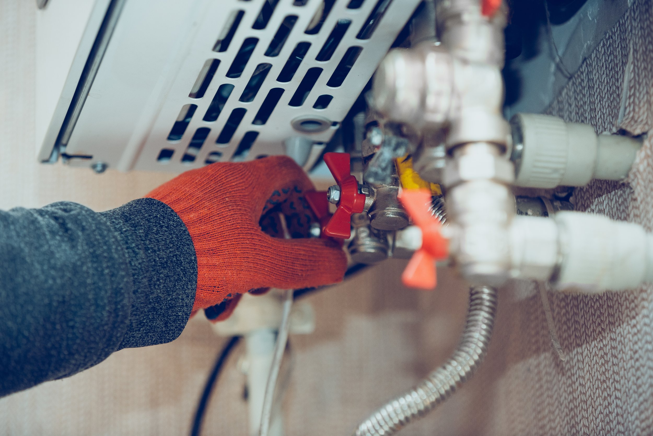 A person wearing an orange glove turning a valve on a plumbing system with various pipes and fittings.