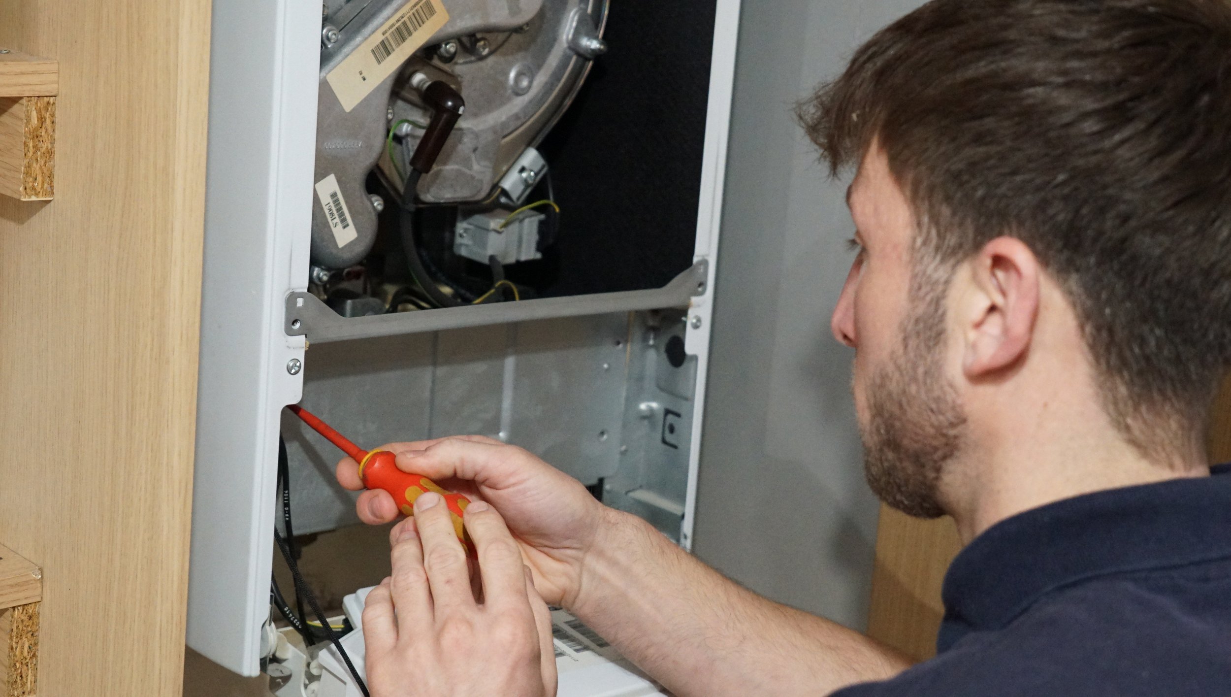 A technician repairing or installing a piece of electrical or electronic equipment inside a metal enclosure, using a screwdriver.