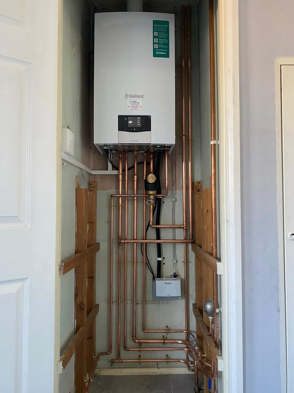 A wall-mounted hot water heater with copper plumbing pipes and a digital thermostat in a utility closet.
