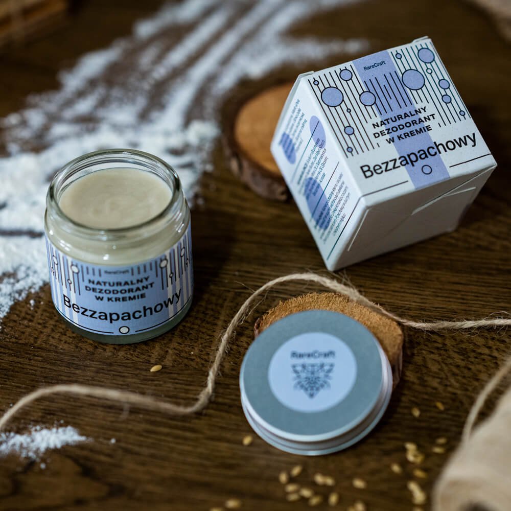 Naturalny-dezodorant-w-kremie-w-szklanym-sloiczku-z-niebieska-etykieta-Bezzapachowy-obok-opakowania-w-niebiesko-bialej-grafice-na-tle-drewnianego-stolu-z-bialym-proszkiem,-konopnymi-sznurkami-i-drewnianymi-dekoracjami..jpg