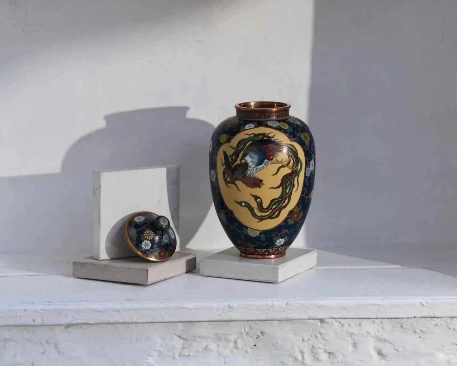 Decorative Asian-style vase with dragon design, accompanied by a small matching bowl, placed on white platforms against a light background.