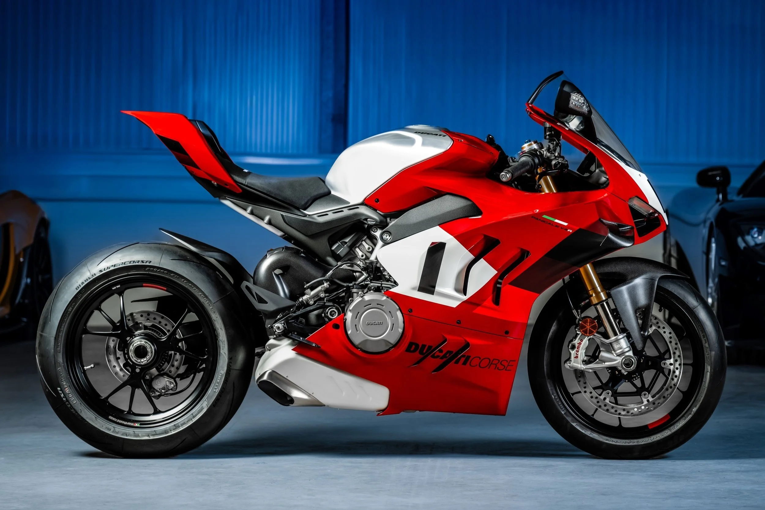 Red and white Ducati motorcycle parked indoors, with a blue wall in the background.
