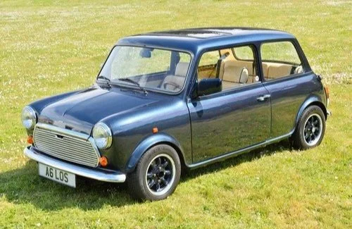 a classic Mini Cooper car parked on grass, painted in dark blue with a beige interior visible through the windows