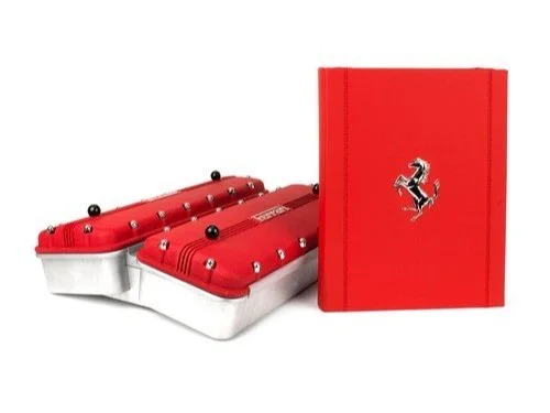 A red Ferrari-themed lunchbox with a book or notebook featuring the Ferrari logo.
