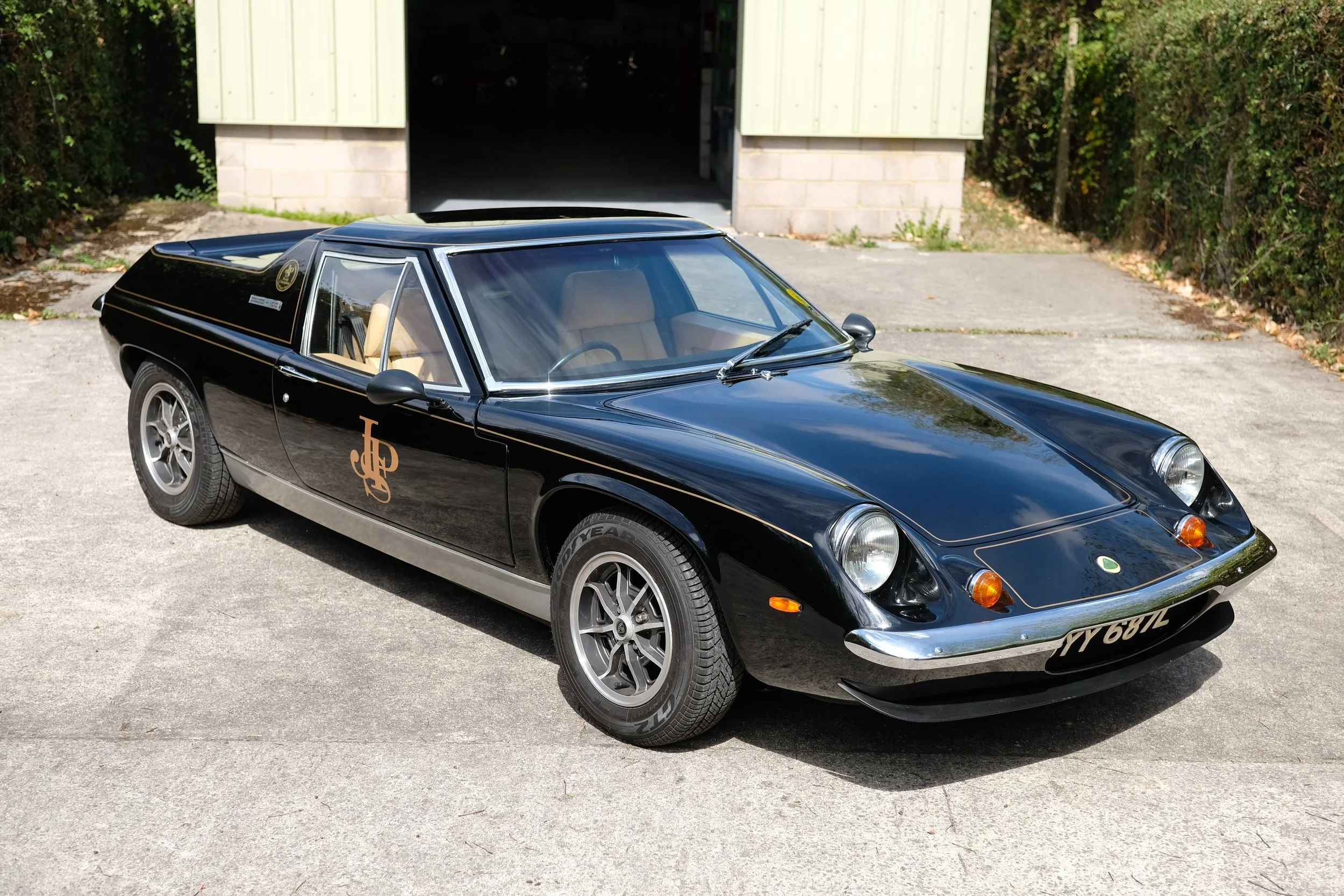 Black vintage sports car with gold lettering parked on driveway in front of a garage