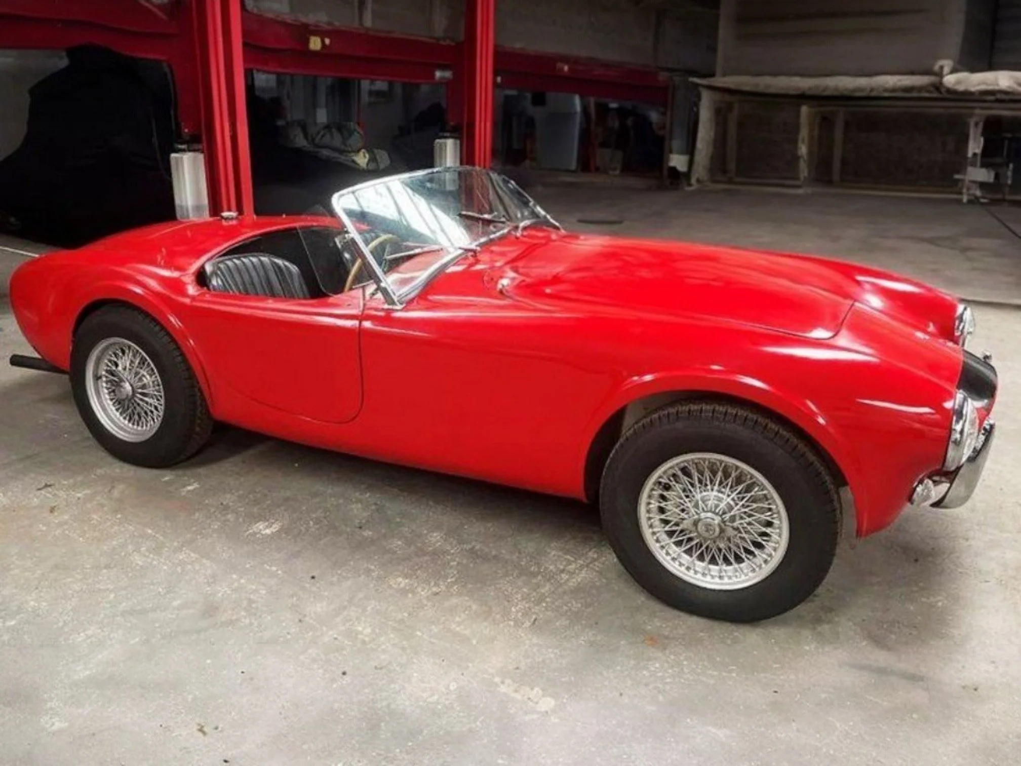 A vintage red convertible sports car parked in a garage or workshop.