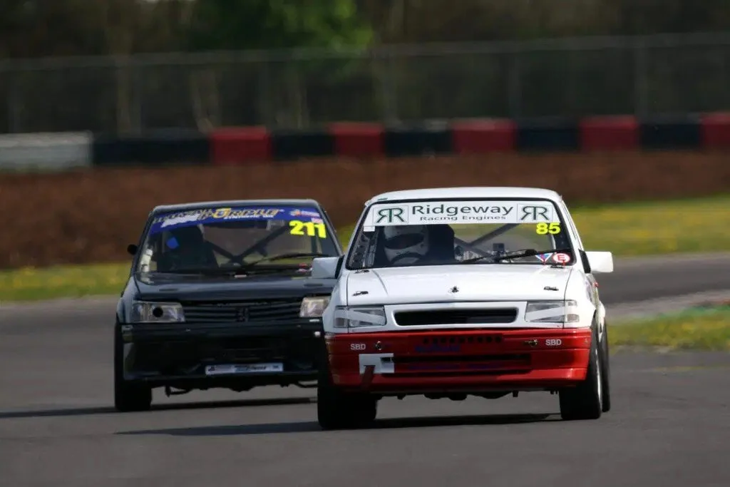 Two race cars on a track, one white and one black, racing side by side.