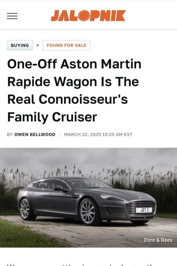 A dark gray Aston Martin Rapide Wagon with a front license plate reading 'JET 2', parked outdoors on a concrete surface with tall grass and dark clouds in the background.